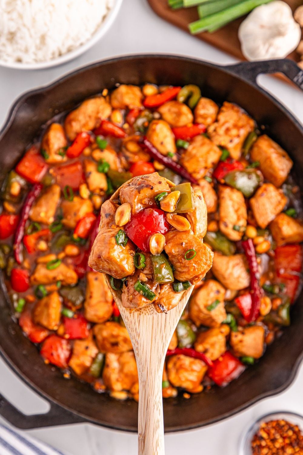Better Than Takeout Kung Pao Chicken in a skillet with a wooden spoon scooping out of it