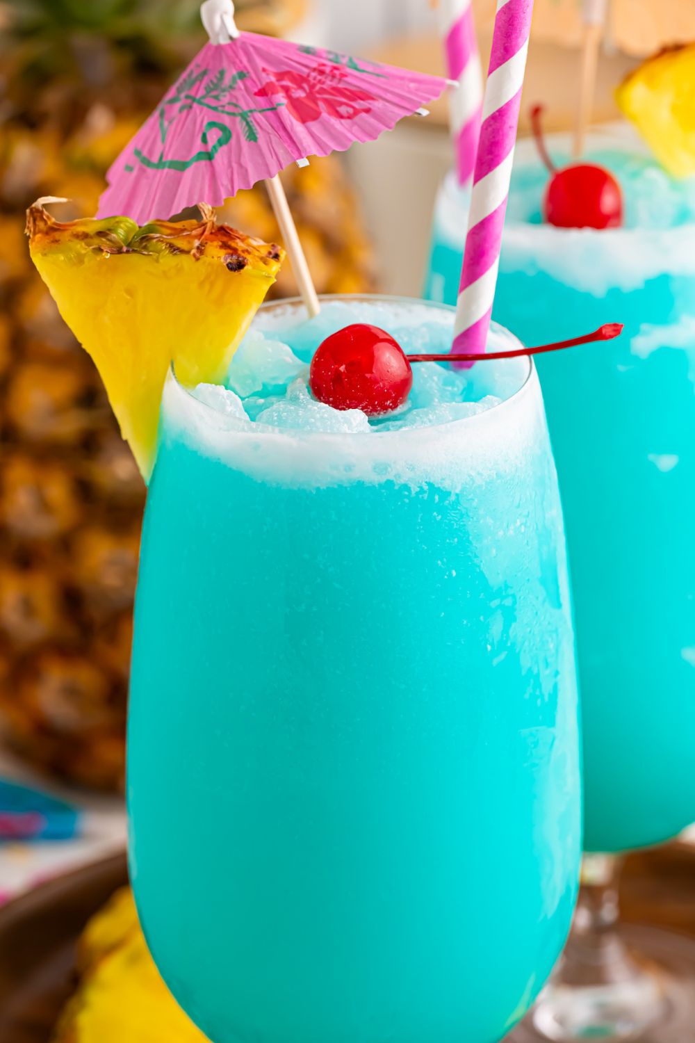 close up of Frozen Blue Hawaiian Cocktails in glasses with coconut rim, pineapple wedge and maraschino cherry 