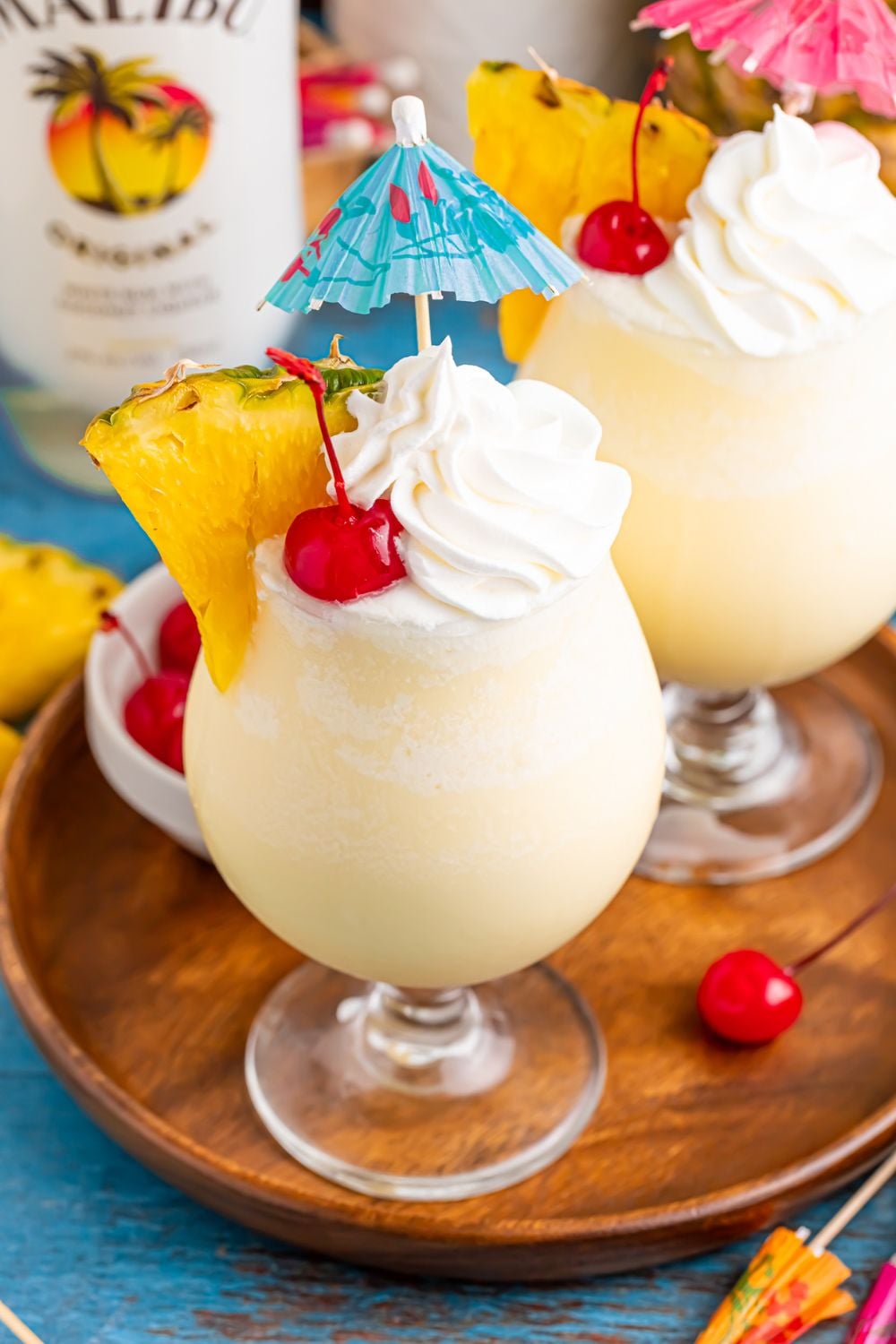 Frozen Malibu Piña Colada on table with pineapple wedges and whipped cream and umbrella topper