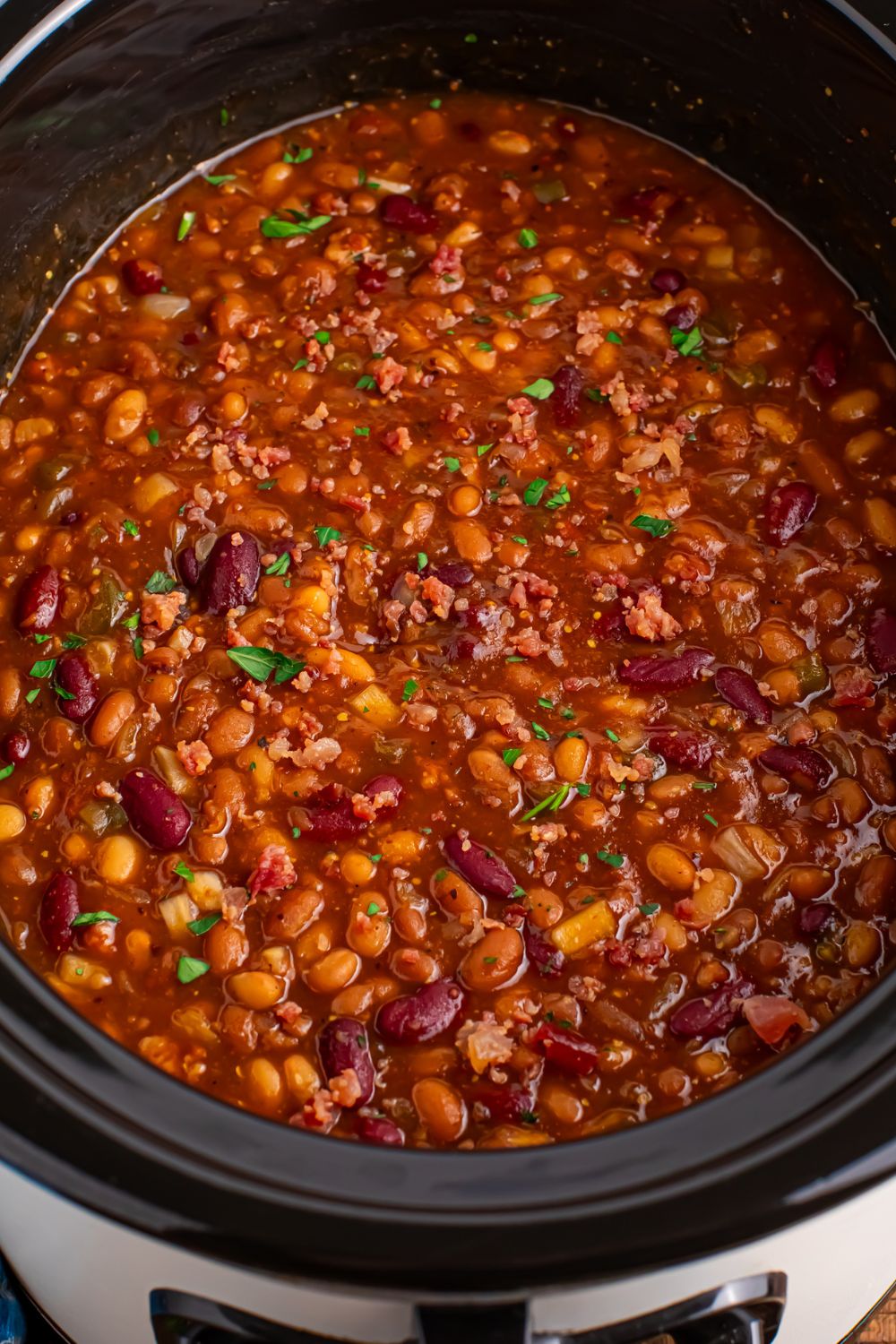 Crockpot bourbon baked beans in a crockpot with a sprinkle of parsley on top