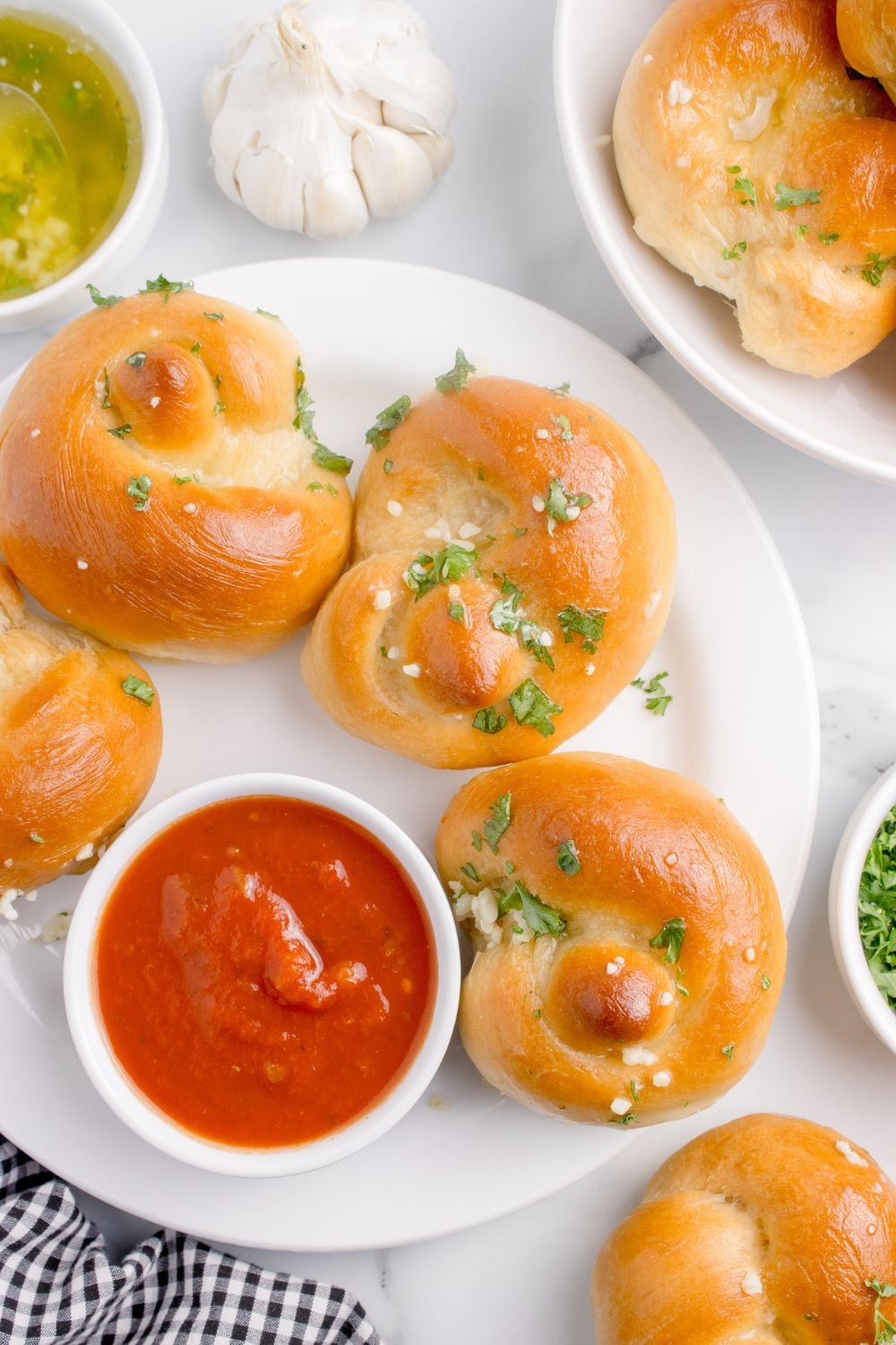 Homemade Garlic Knots on a plate with a bowl of marinara on side and garlic butter 