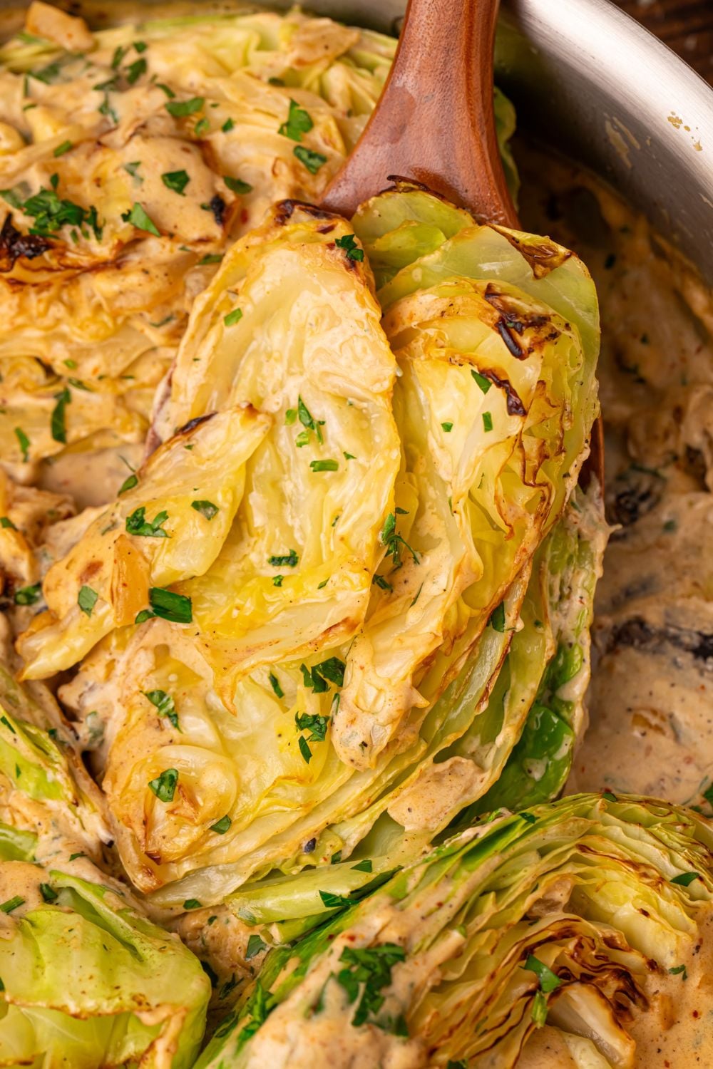 Creamy Garlic Parmesan Cabbage in a skillet with one being lifted out with a spoon 