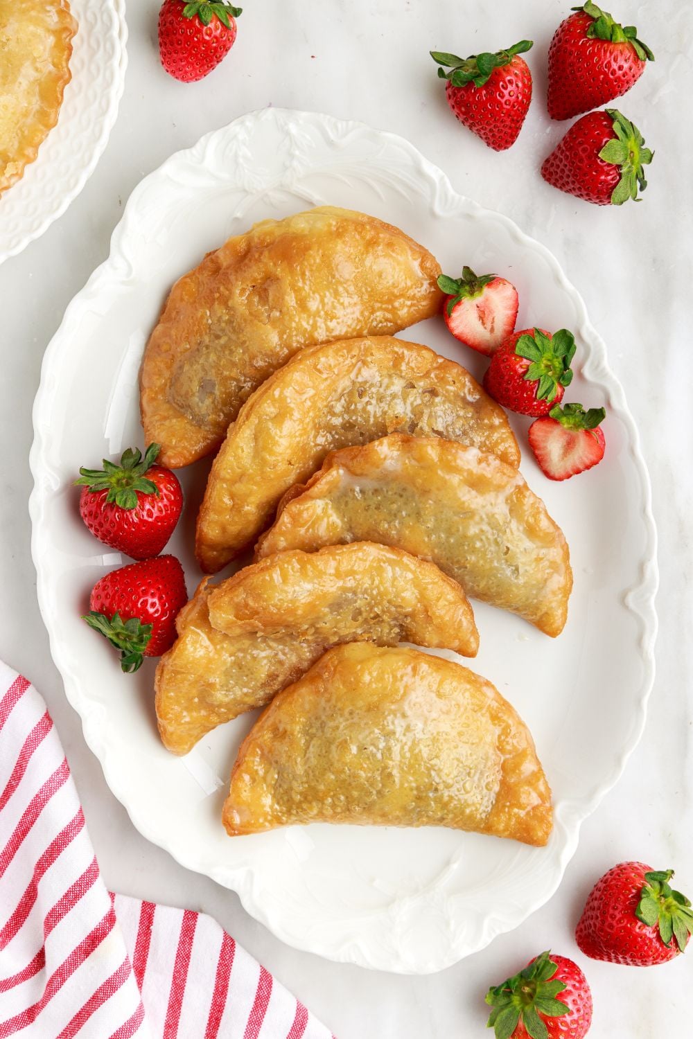 Deep Fried Strawberry Cheesecake Pies on a tray with strawberries scattered around the table with a red striped towel to side