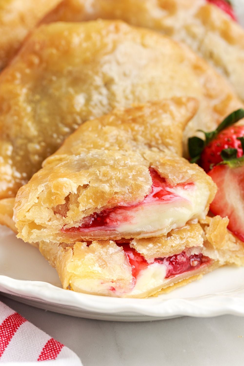 Deep Fried Strawberry Cheesecake Pies on a platter with one cut in half to show the filling inside the pies