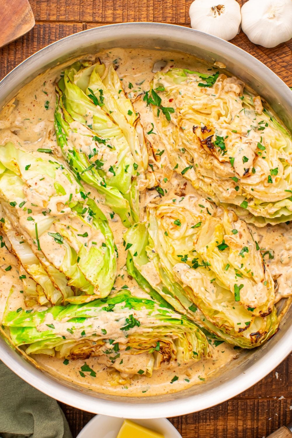 Creamy Garlic Parmesan Cabbage in a skillet on table with garlic bulbs to side 