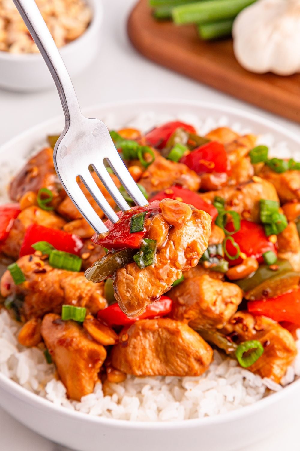 Better Than Takeout Kung Pao Chicken on plate with a bed of rice under chicken and a fork sticking in the chicken