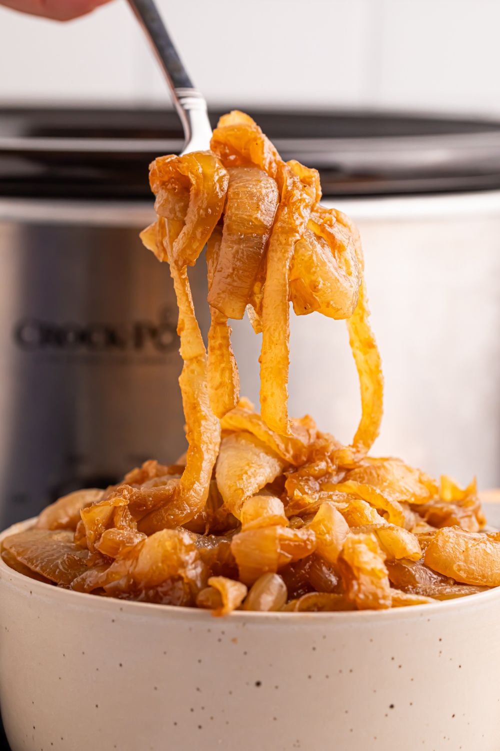 CrockPot Caramelized Onions and a bowl in front of CrockPot with a spoon lifting up some of the onions