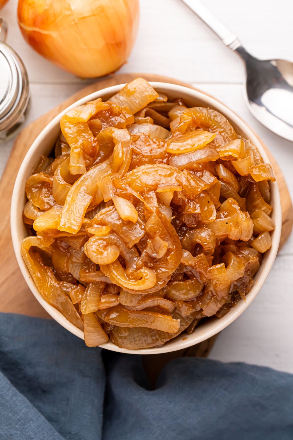 CrockPot Caramelized Onions in a bowl with an onion and a spoon to the side of spoon on table