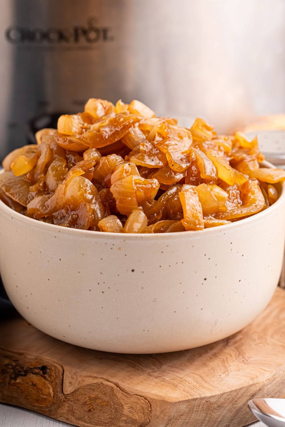 CrockPot Caramelized Onions in a white bowl on table with a CrockPot behind it on table