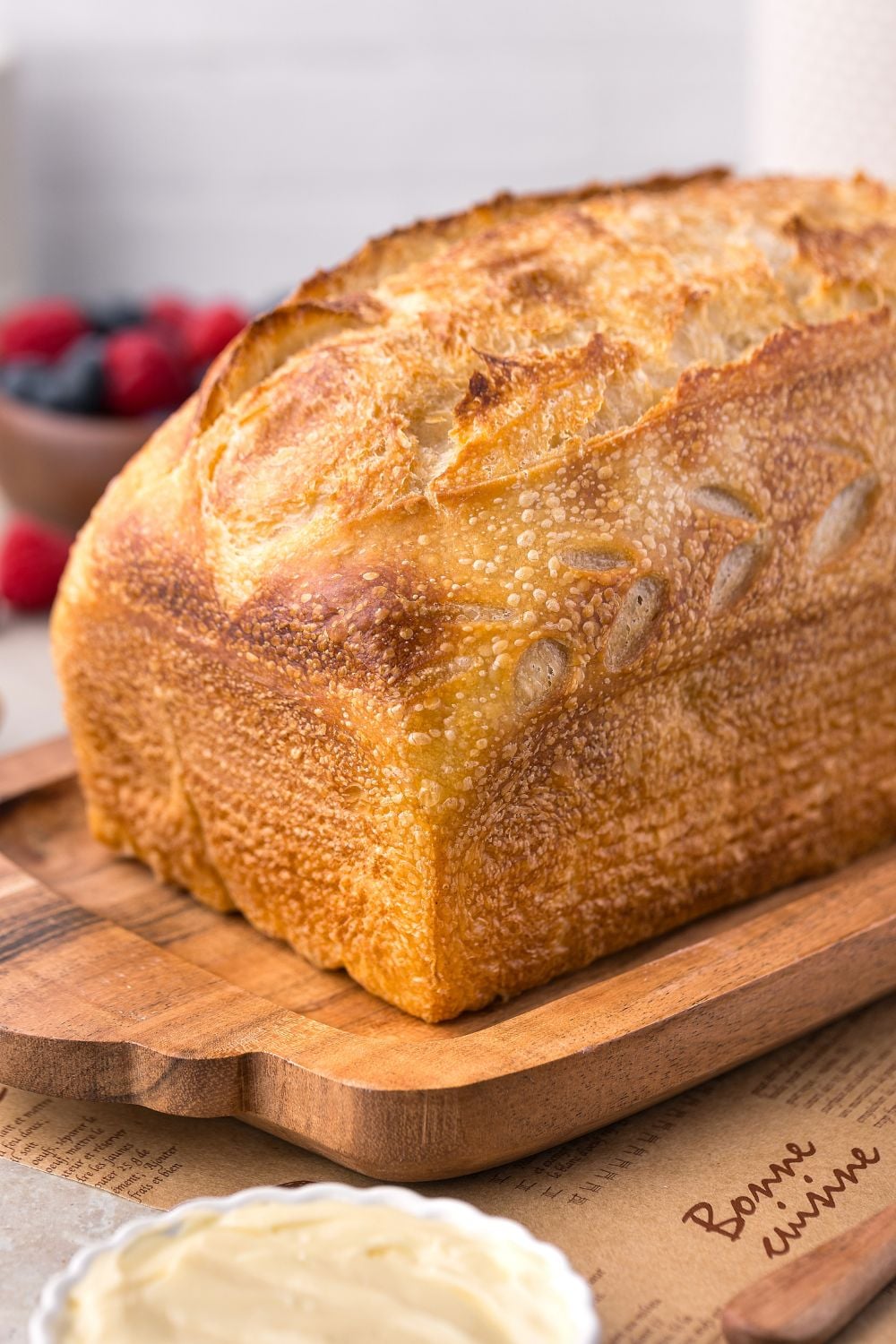 Homemade Sourdough Bread sitting on a cutting board with berries in a bowl to the side of table 