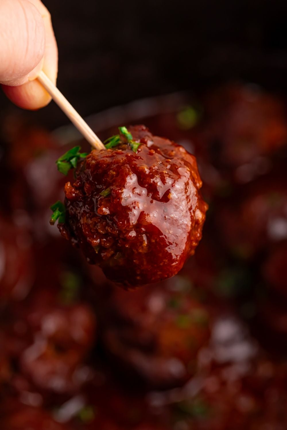 toothpick with a homemade bbq meatball on it above Crockpot