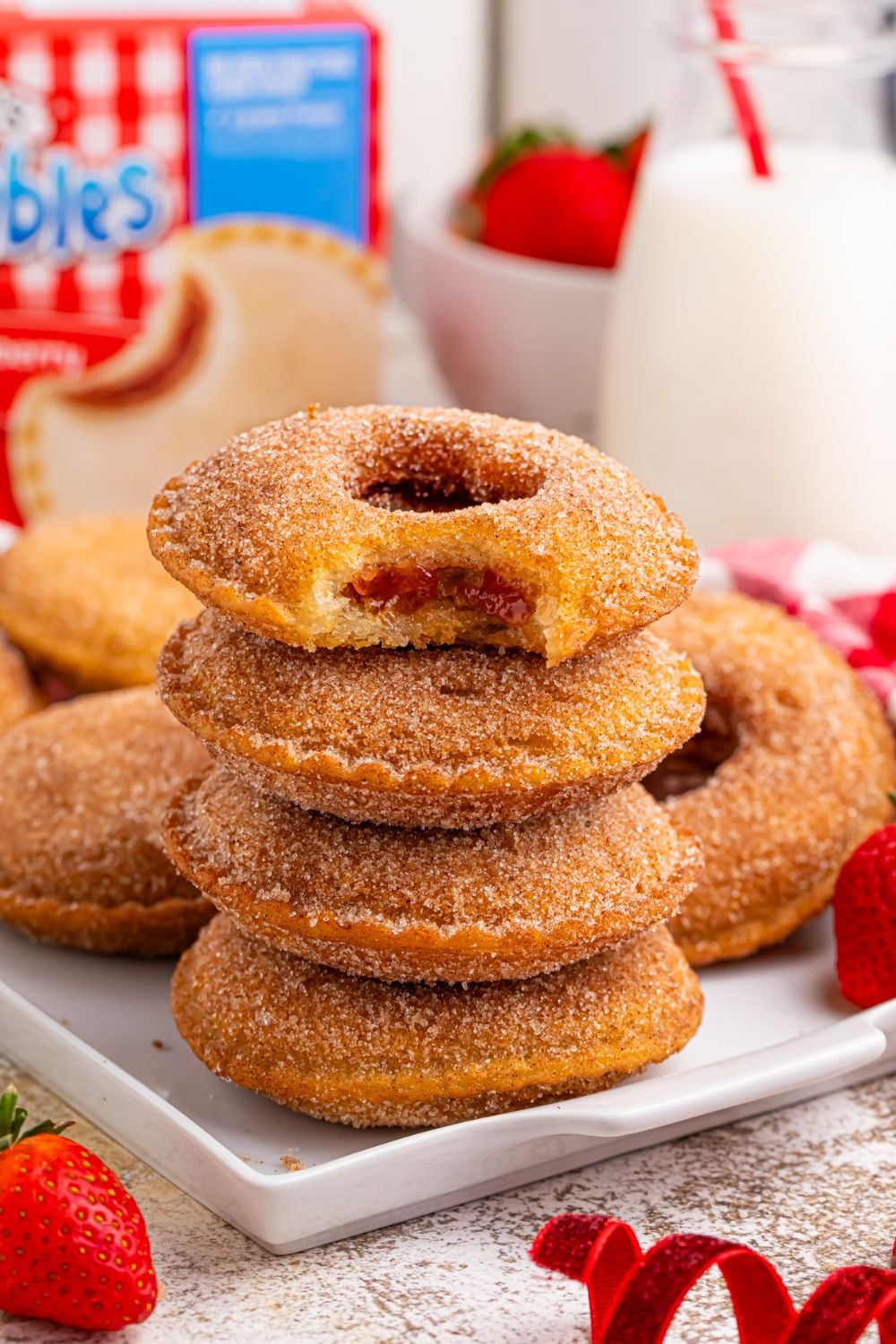 stack of fried uncrustables on plate with more behind it and a tall glass of milk and uncrustable box behind it on table
