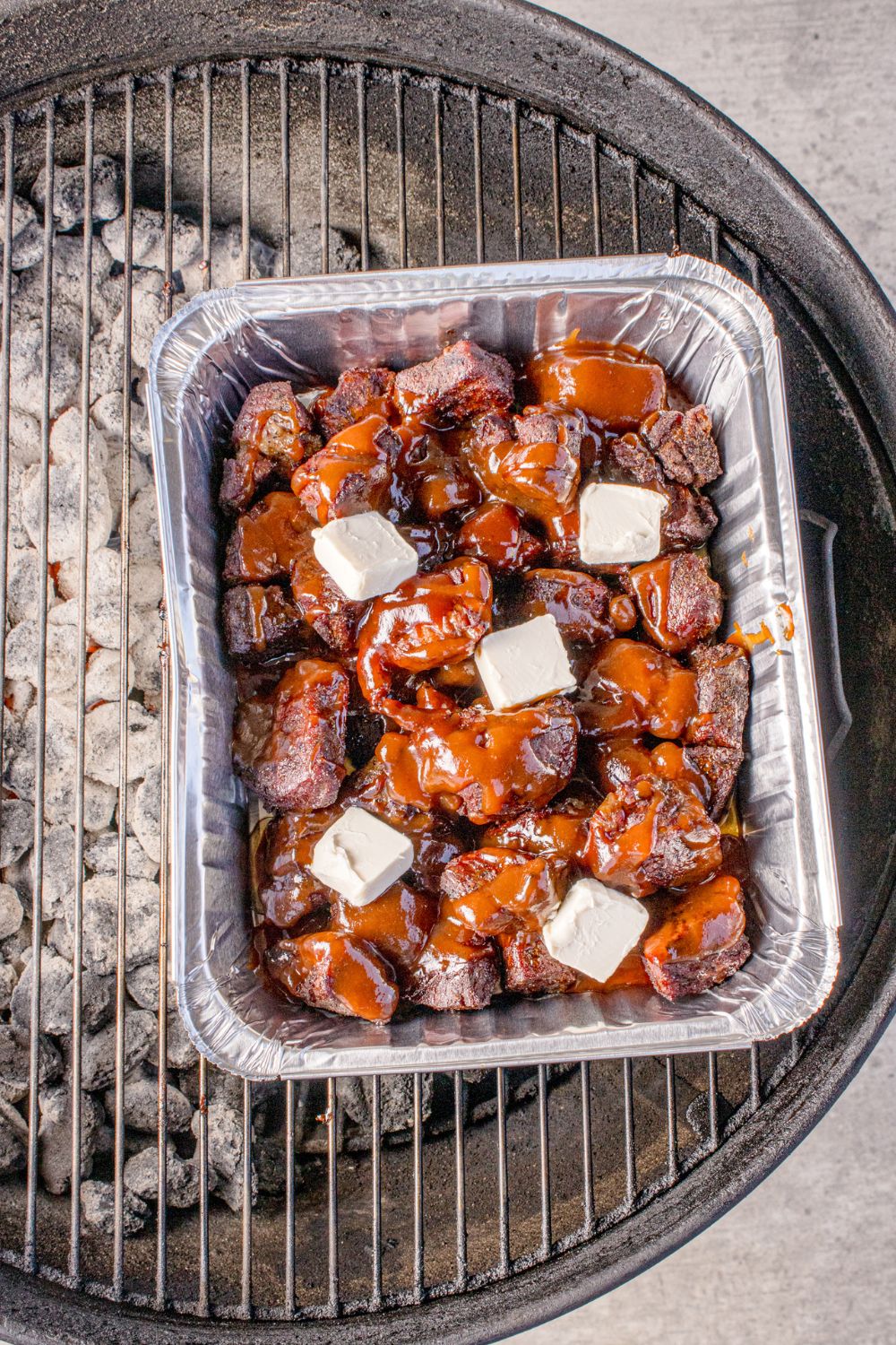 Chuck Roast Burnt Ends in a pan on charcoal grill with butter on top