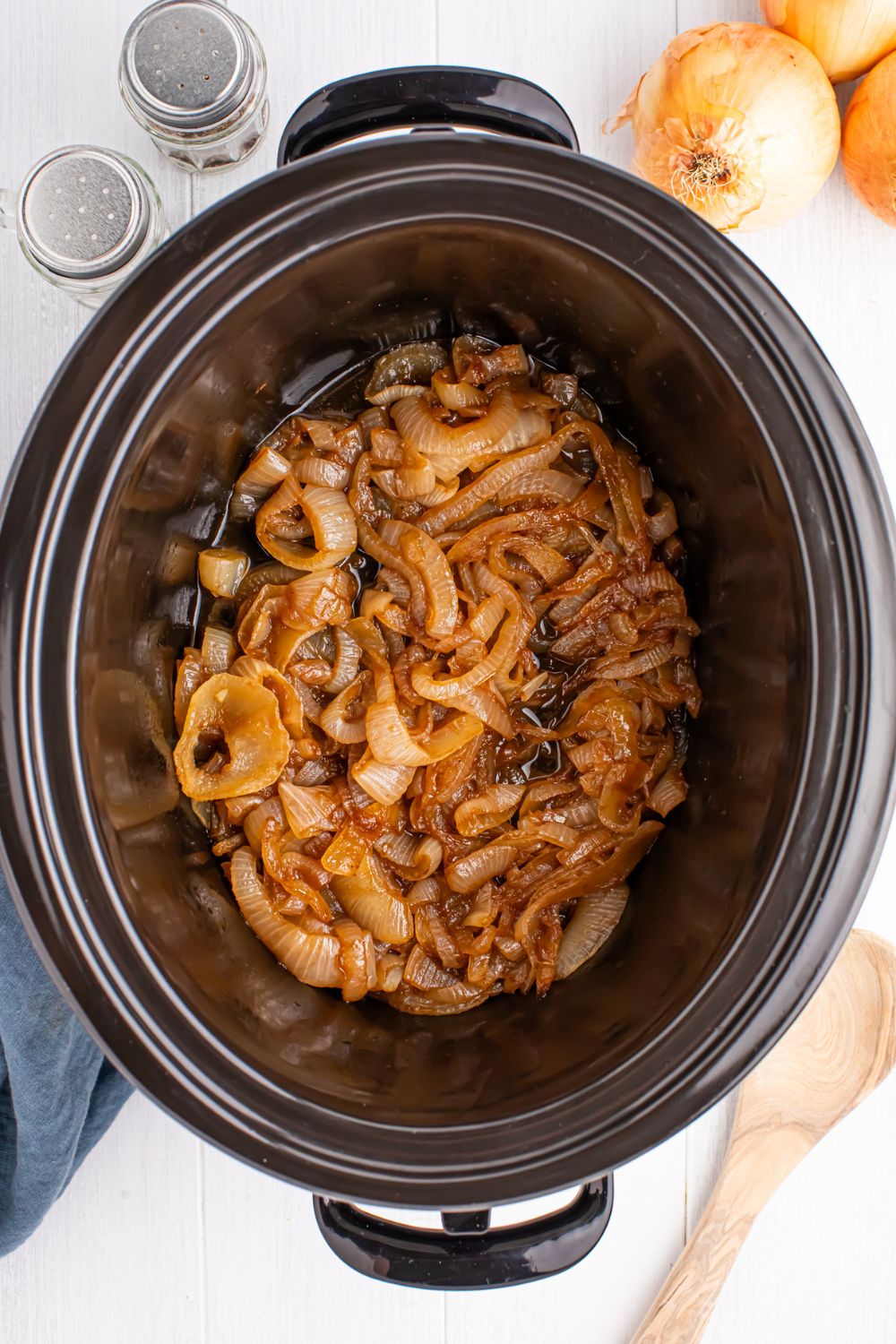 overhead look of CrockPot Caramelized onions on table with onions and salt and pepper to side