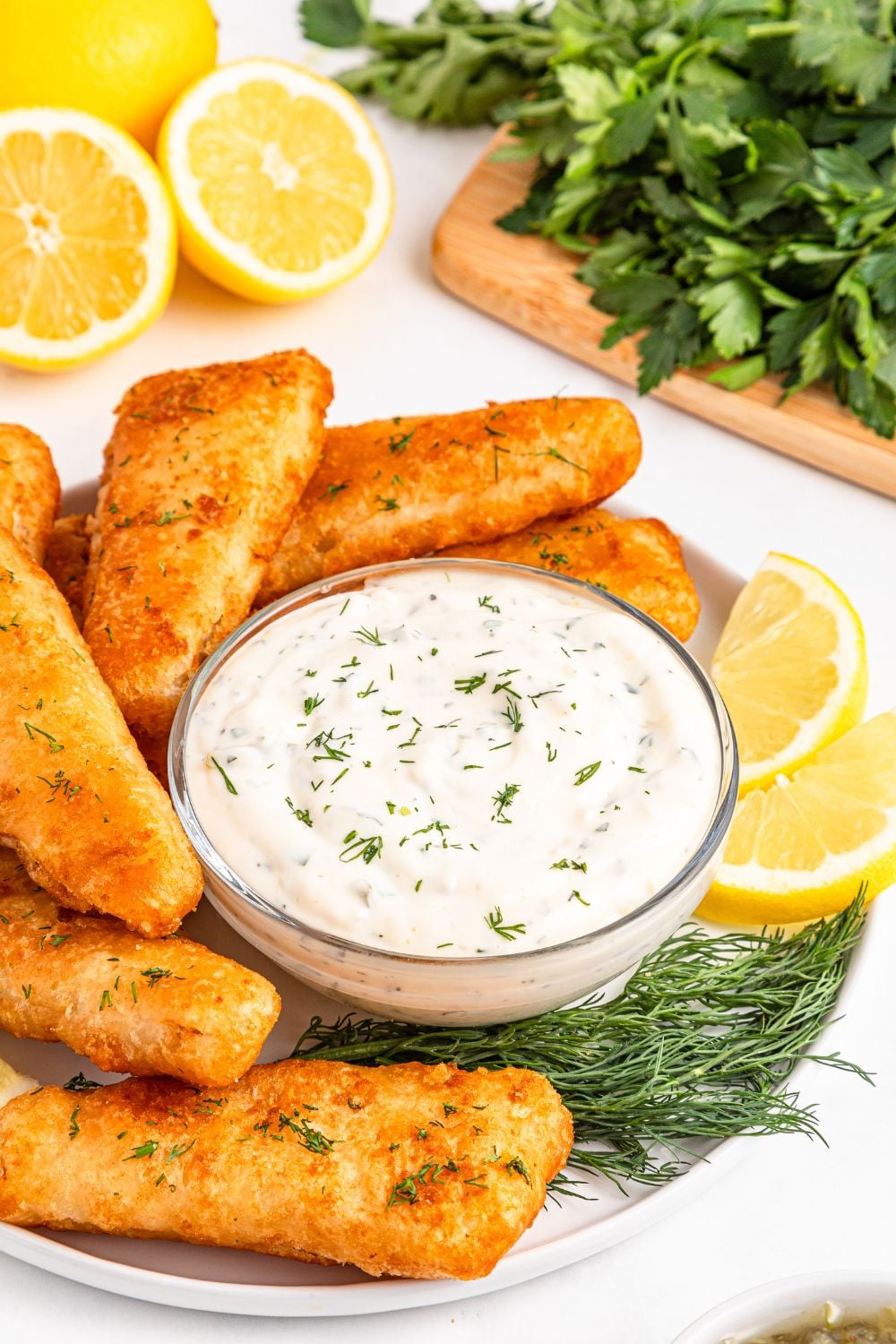 Easy Homemade Tarter Sauce in a glass jar with fish fillets on table with lemon wedges to side