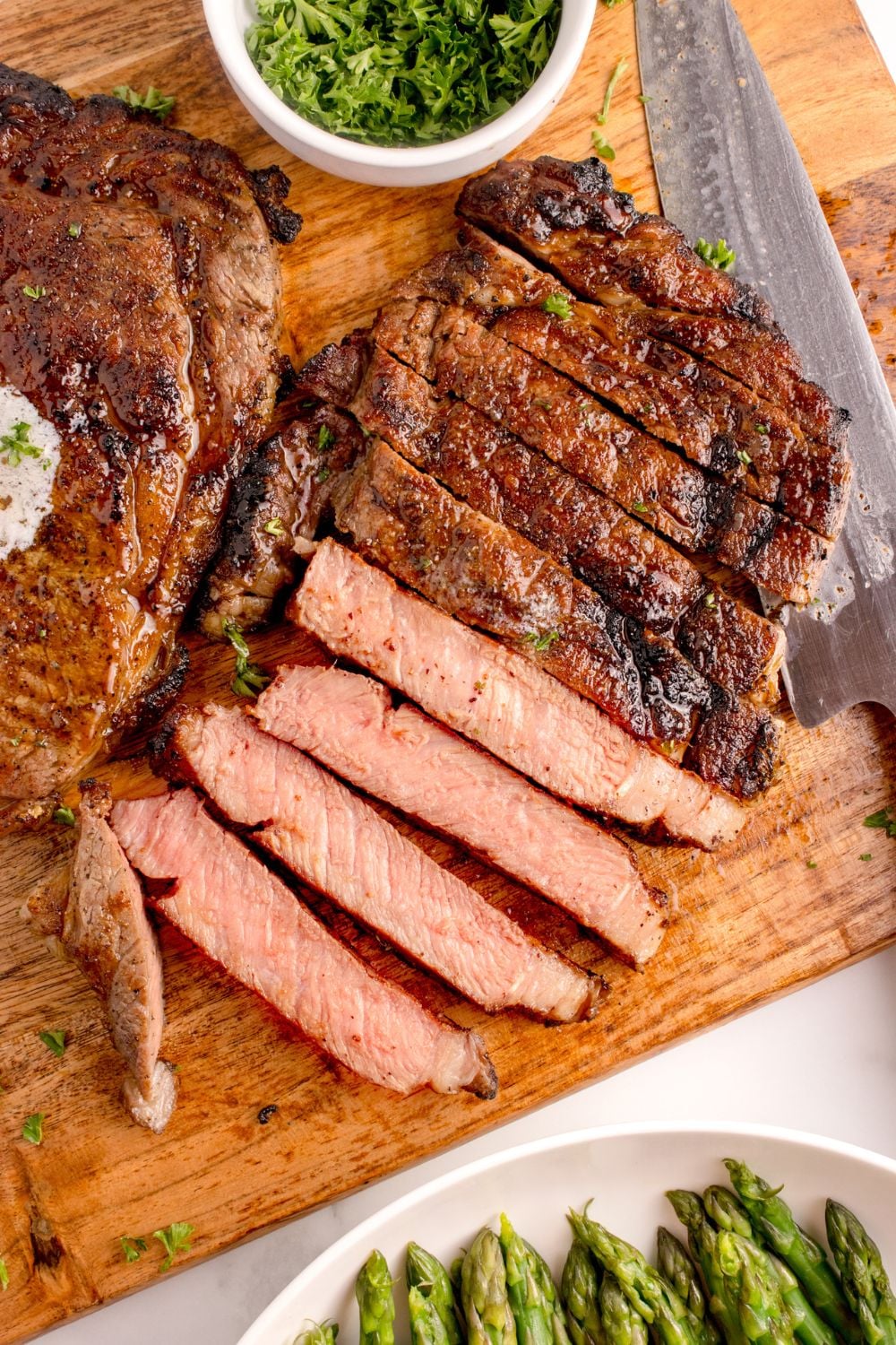 Grilled Ribeye Steak sliced into strips on cutting board with a whole steak to side