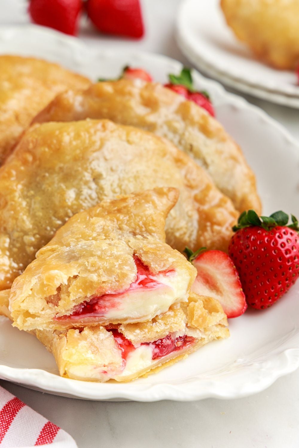 Deep Fried Strawberry Cheesecake Pies laid out on a plate with one torn in half to show the cream cheese and strawberry filling