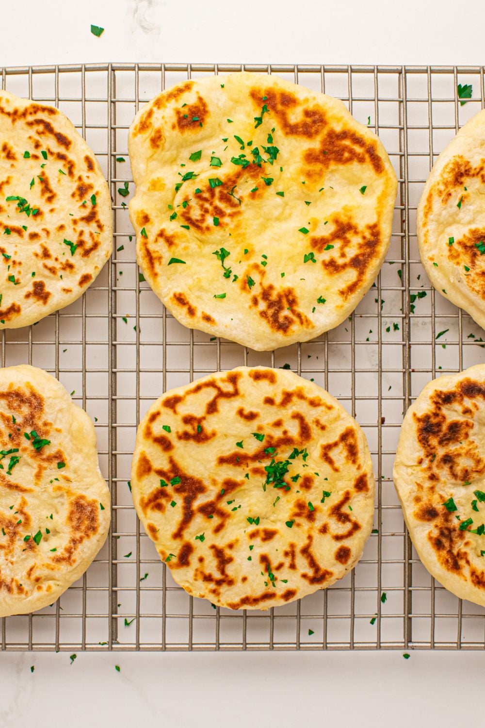3 Ingredient Flatbreads spread out on cooling rack topped with butter and parsley flakes