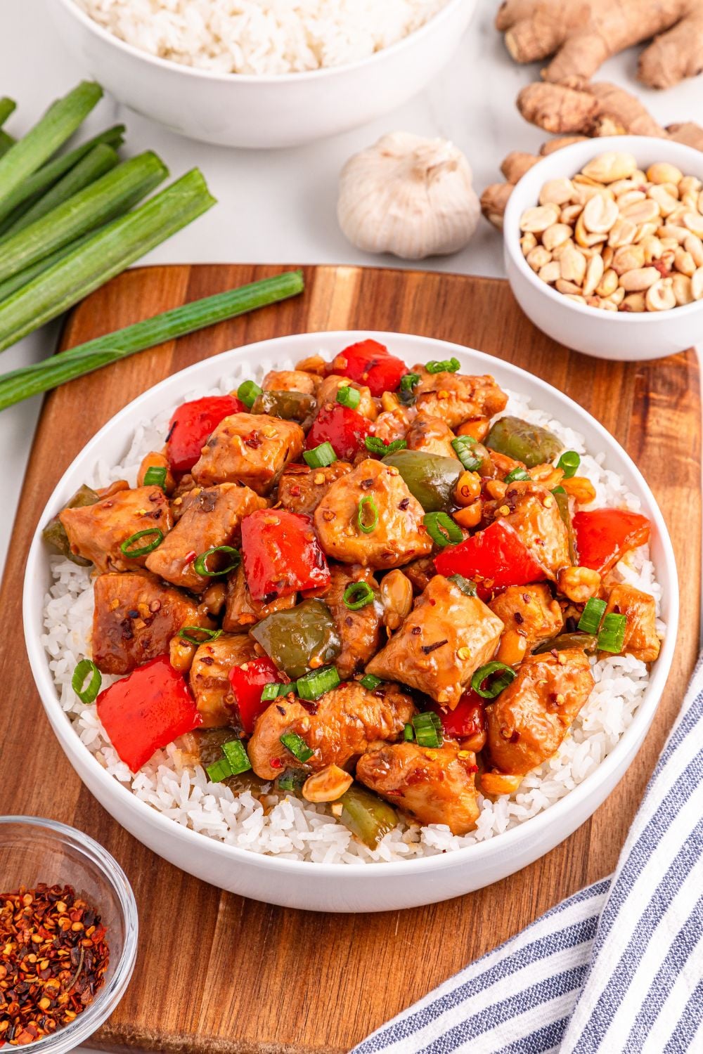 Better Than Takeout Kung Pao Chicken on a plate with rice and chicken, and green onions and garlic to the side of plate