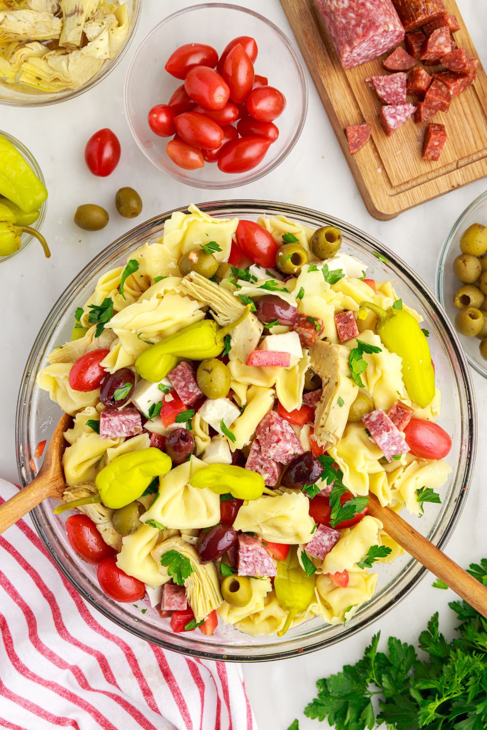 Antipasto Tortellini Pasta Salad in a bowl with peppers and tomatoes around the bowl of pasta 
