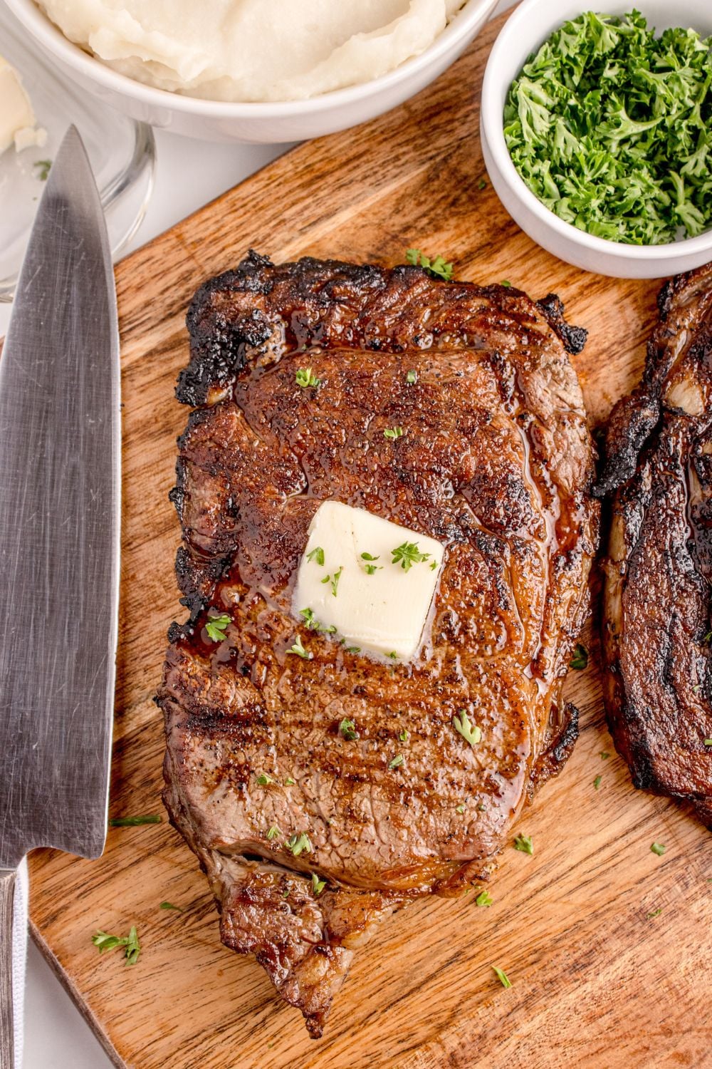 butter on top of Grilled Ribeye Steak on cutting board with knife sitting next to it on counter
