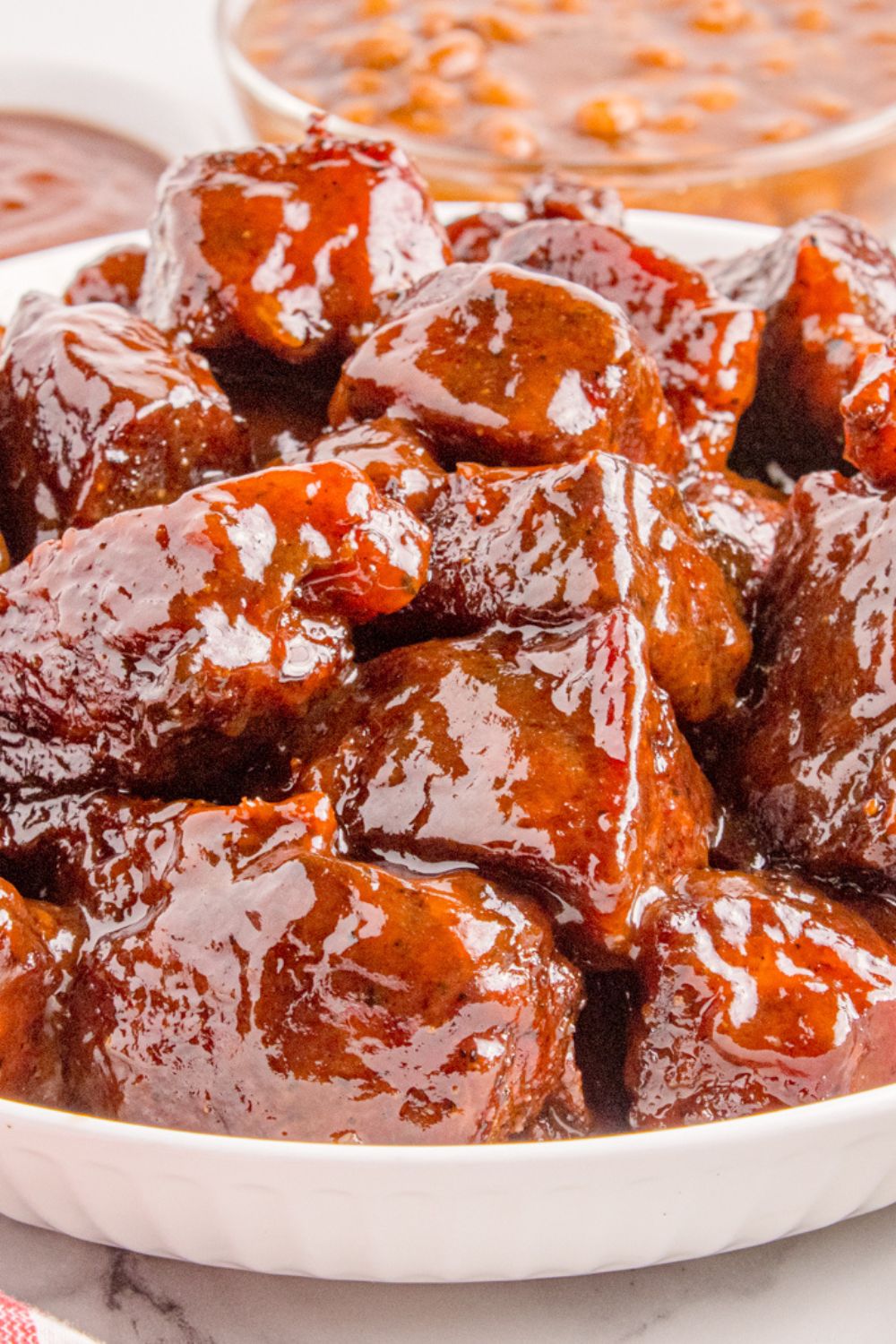 Chuck Roast Burnt Ends in a white bowl on a table with a bowl of beans to the side