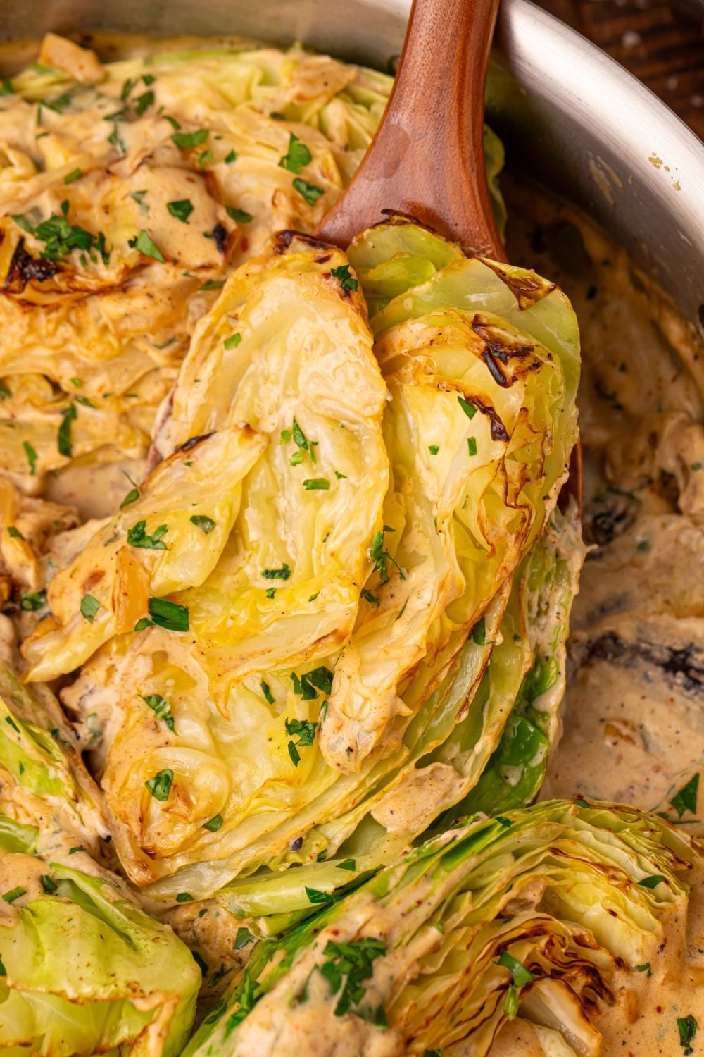 Creamy Garlic Parmesan Cabbage in a skillet being lifted out with a wooden spoon 