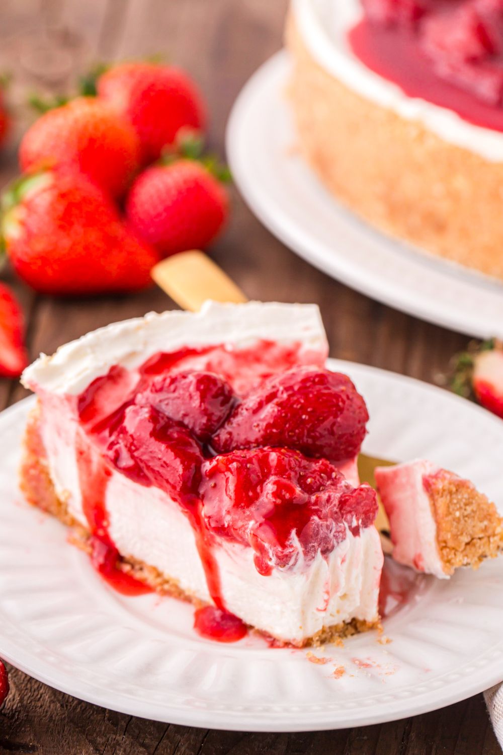 slice of No Bake Strawberry Cheesecake with a bite taken out of it sitting on plate with fresh strawberries in the background