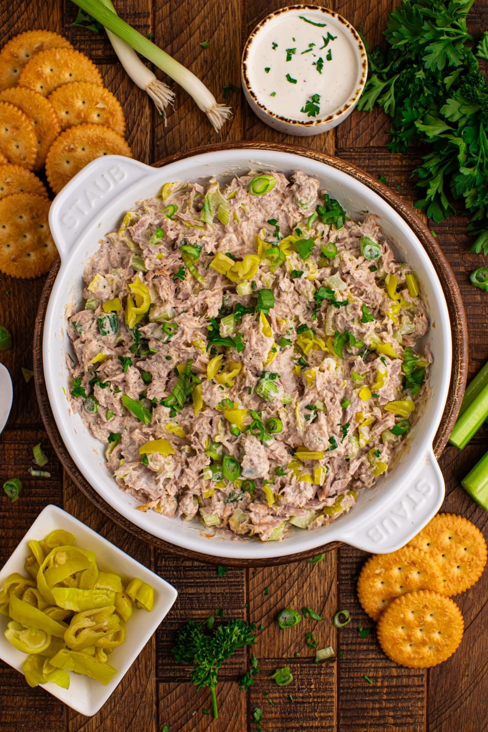 Pepperoncini Ranch Tuna Salad in a bowl with peppers in a bowl, crackers, celery, and more scattered on table 