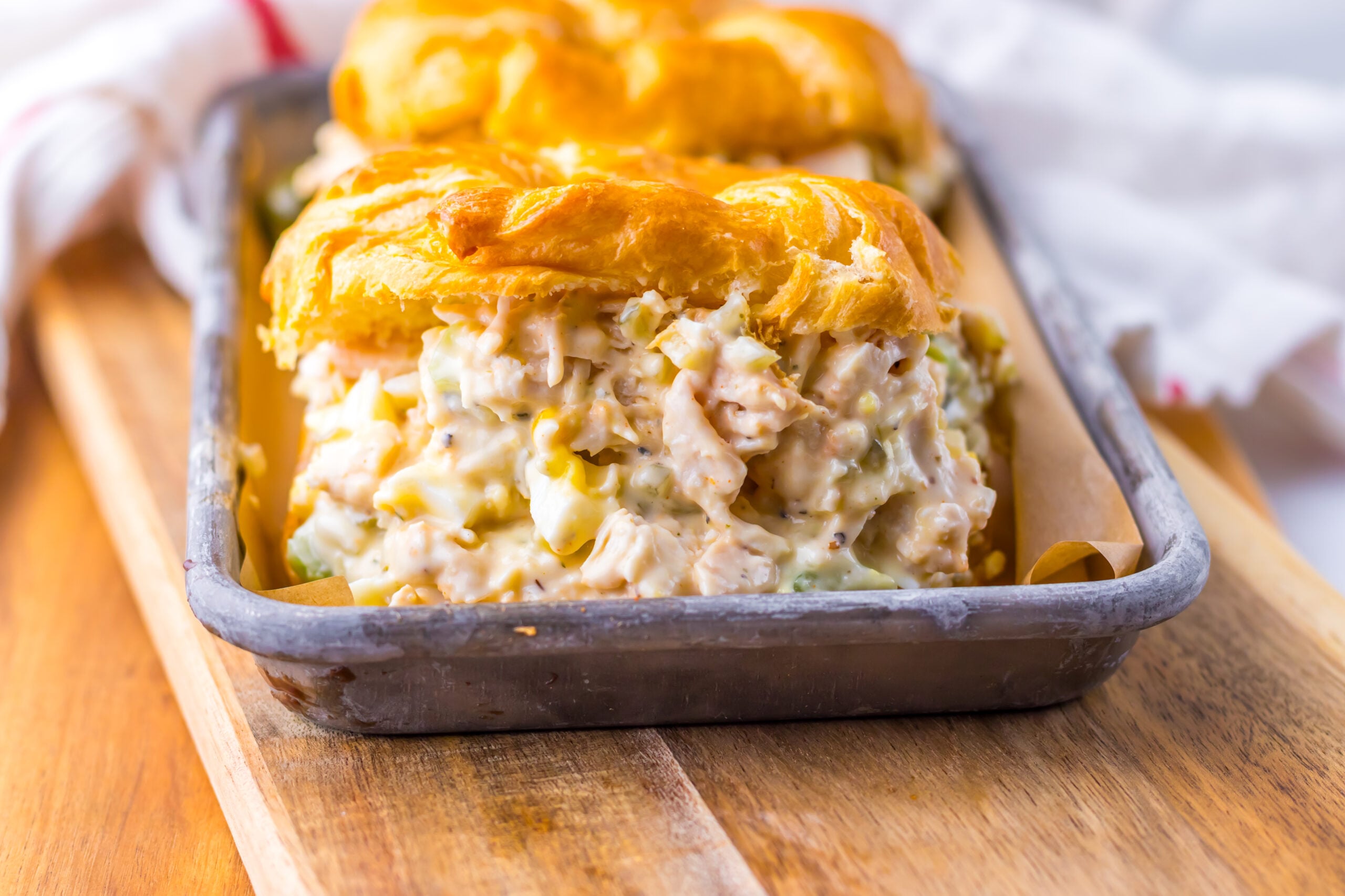 front view of a large chicken salad sandwich on a white croissant on a tin tray. 