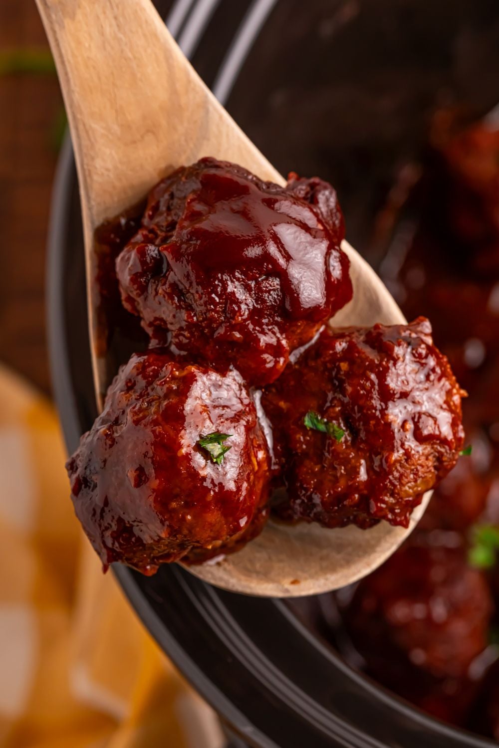 Crockpot Homemade BBQ Meatballs on a wooden spoon lifting up out of crockpot