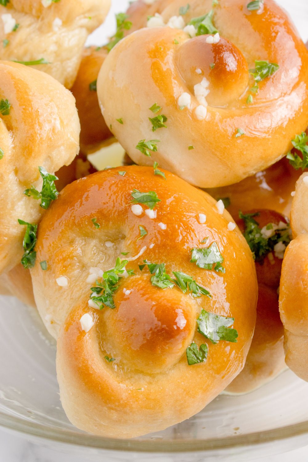 Homemade Garlic Knots on a table topped with garlic and parsley and melted butter 
