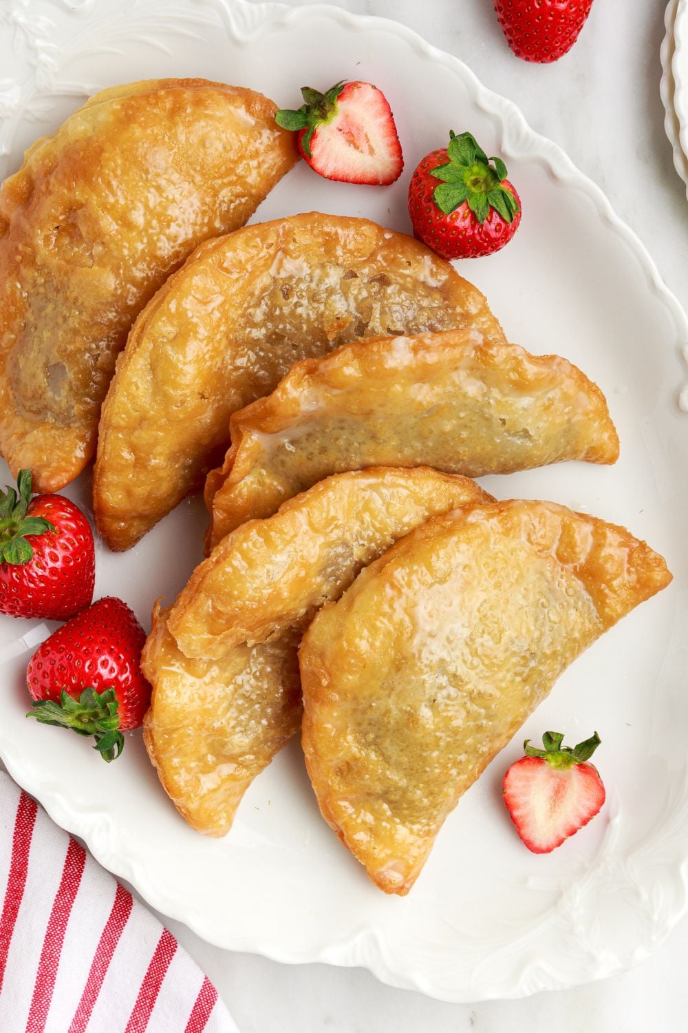 Deep Fried Strawberry Cheesecake Pies placed on tray with fresh berries scattered around the side