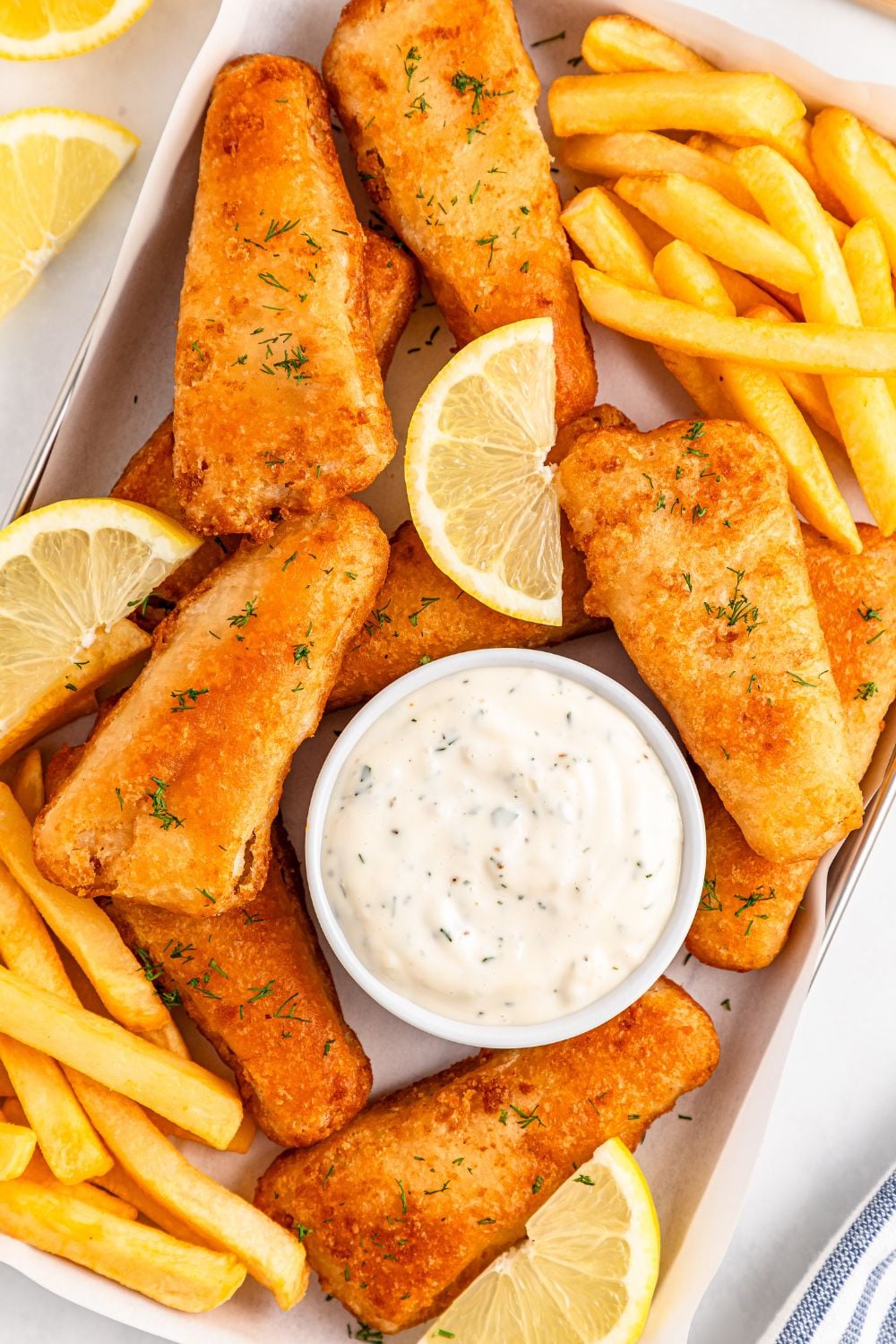 a tray sitting on table with French fries, battered fish, lemon wedges and a bowl of tartar sauce