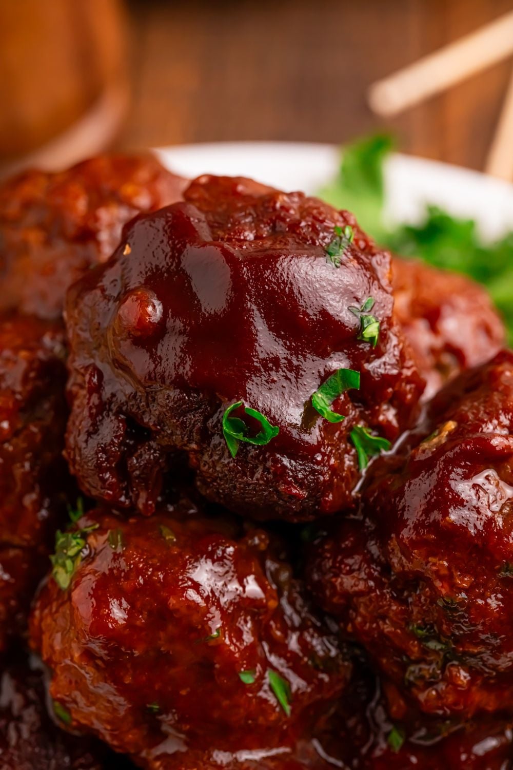 Crockpot Homemade BBQ Meatballs stacked on a plate with some garnish sprinkled on top