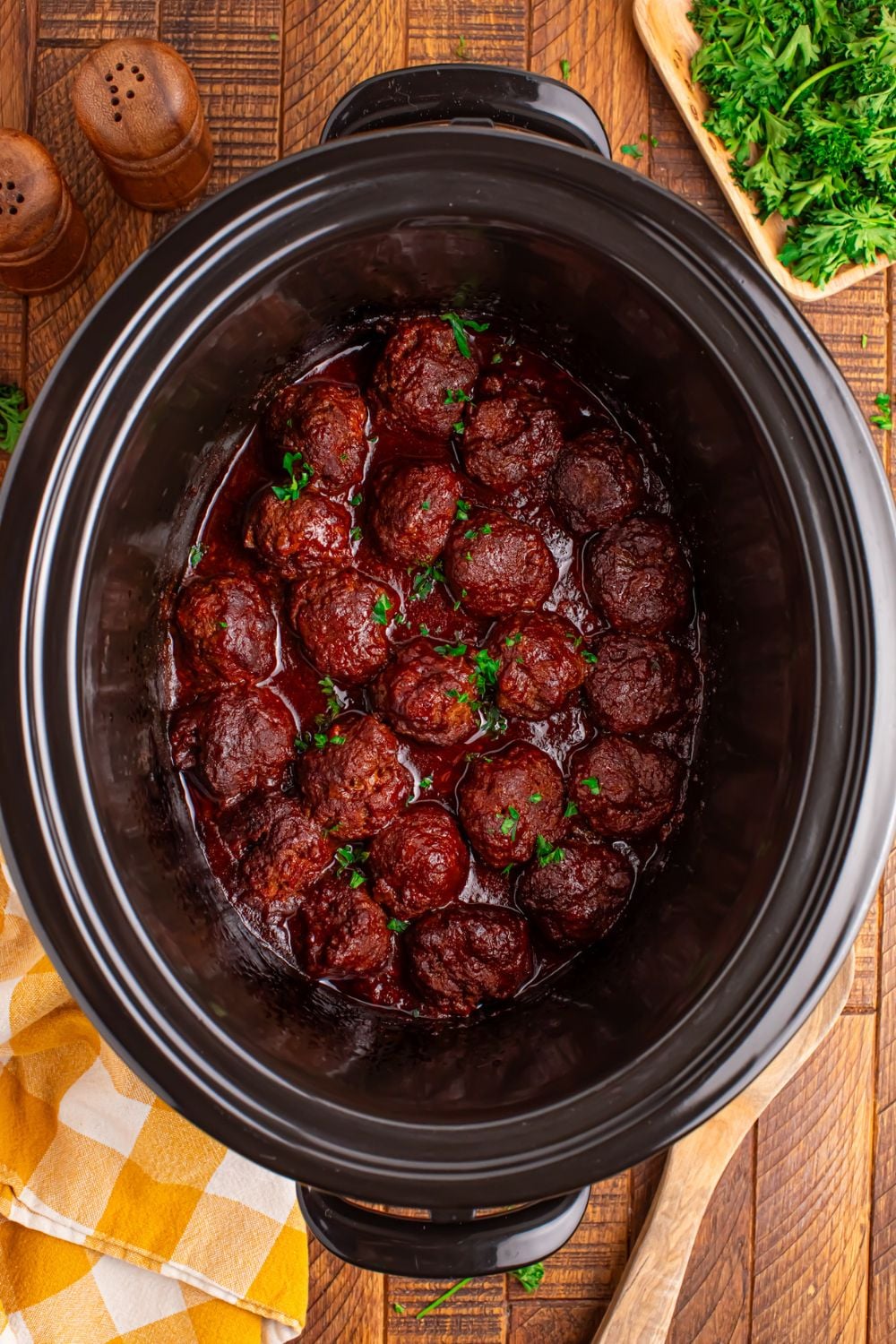 Crockpot Homemade BBQ Meatballs sitting on table with parsley, wooden spoon, and towel to side