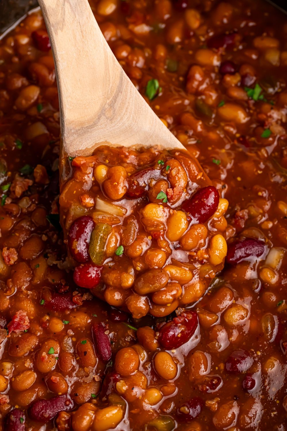 Crockpot Bourbon Brown Sugar Baked Bean in CrockPot with a wooden spoon scooping some out of container