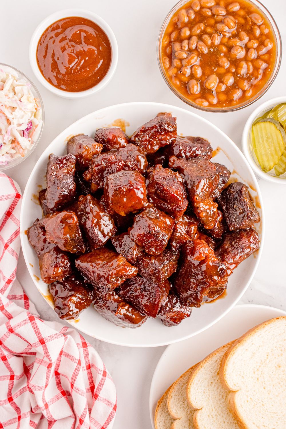 Chuck Roast Burnt Ends in a bowl with a bowl of beans on side, pickles, and sauce around the meat