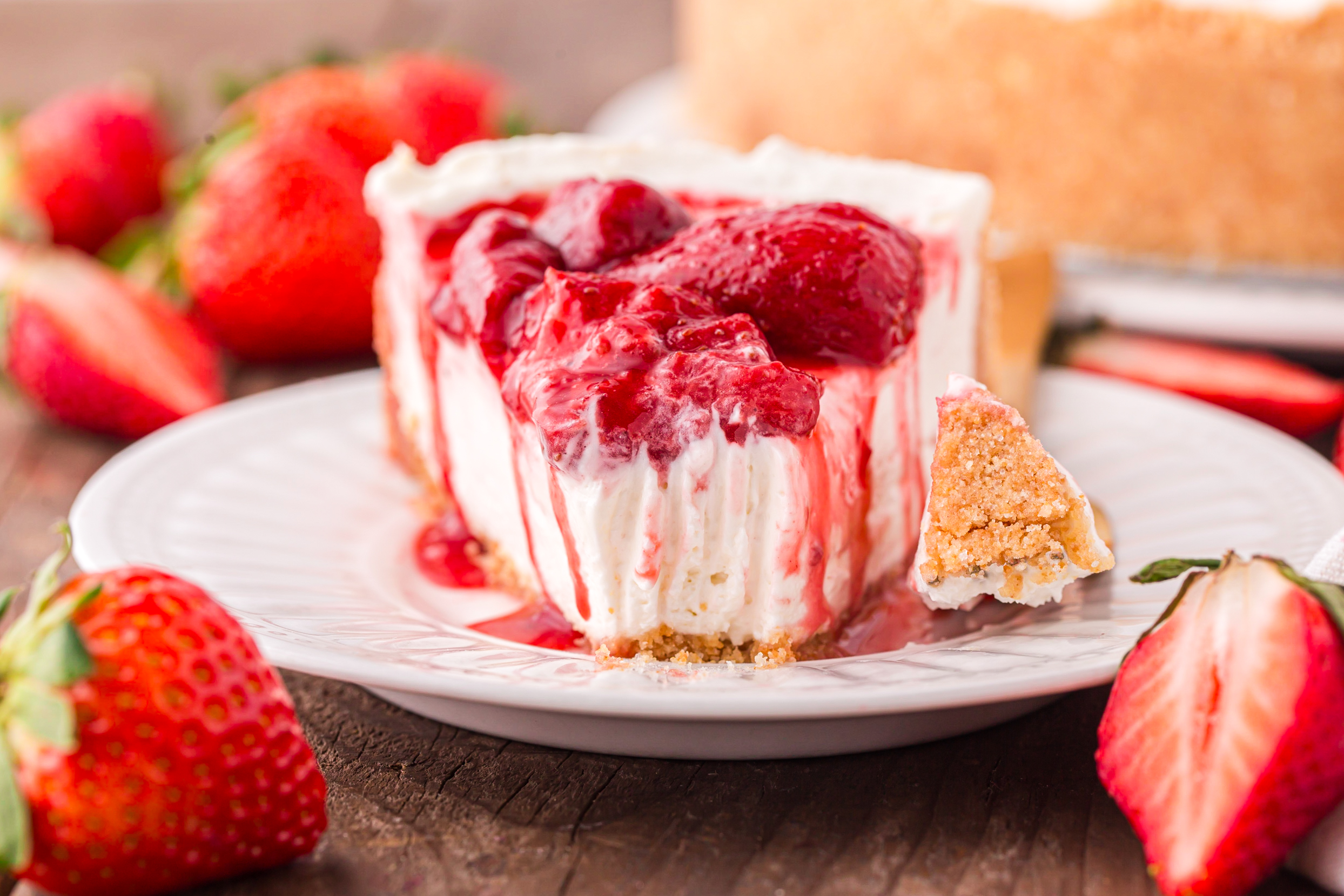 No Bake Strawberry Cheesecake up close on a white plate, topped with juicy strawberries with a bite missing