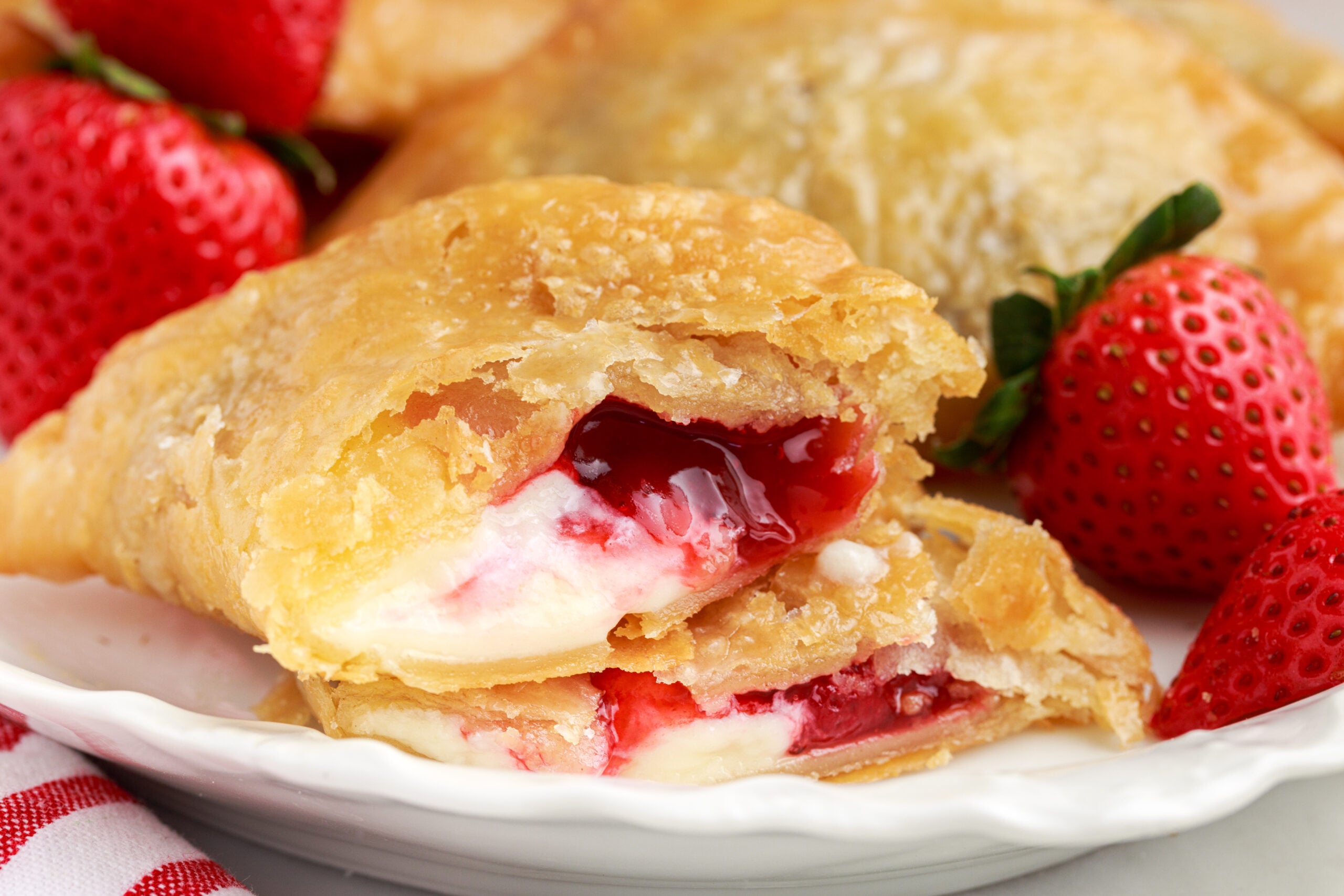 Deep Fried Strawberry Cheesecake Pies on a white dish with one cut open so you can see the inside