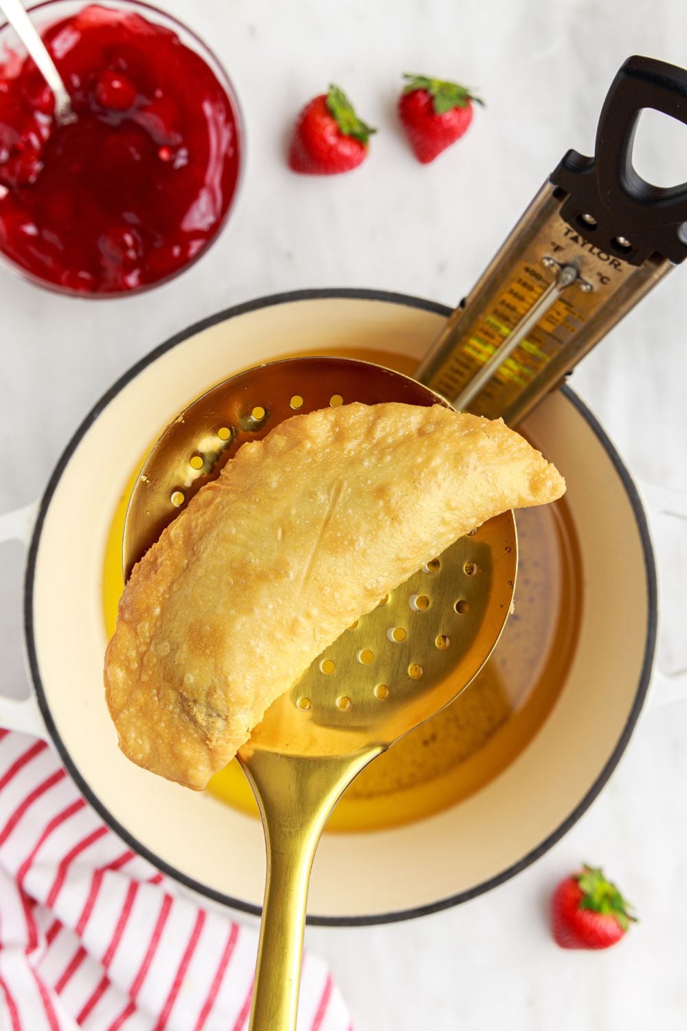 Deep Fried Strawberry Cheesecake Pie above a pot of oil on a ladle