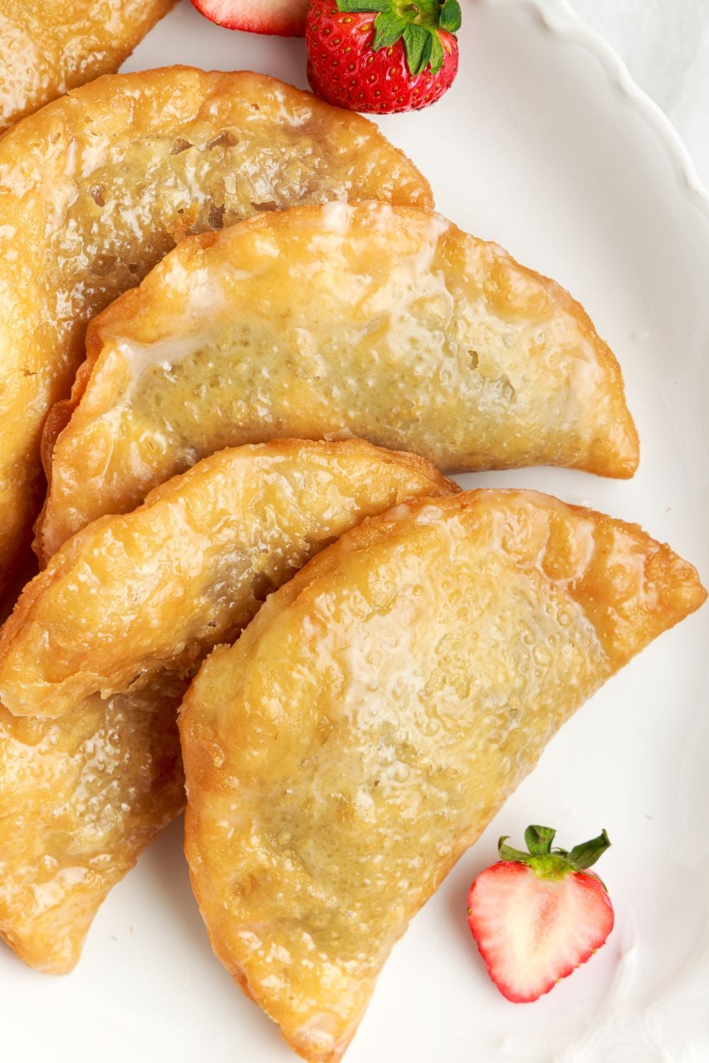 Deep Fried Strawberry Cheesecake Pies laid out on a tray with strawberries around the table