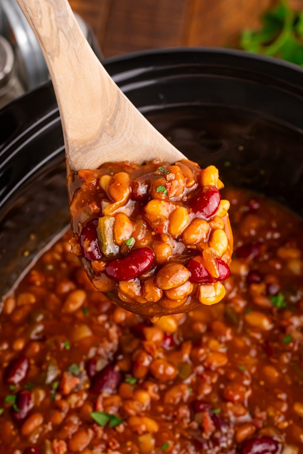 Crockpot bourbon baked beans on a wooden spoon above crockpot on table