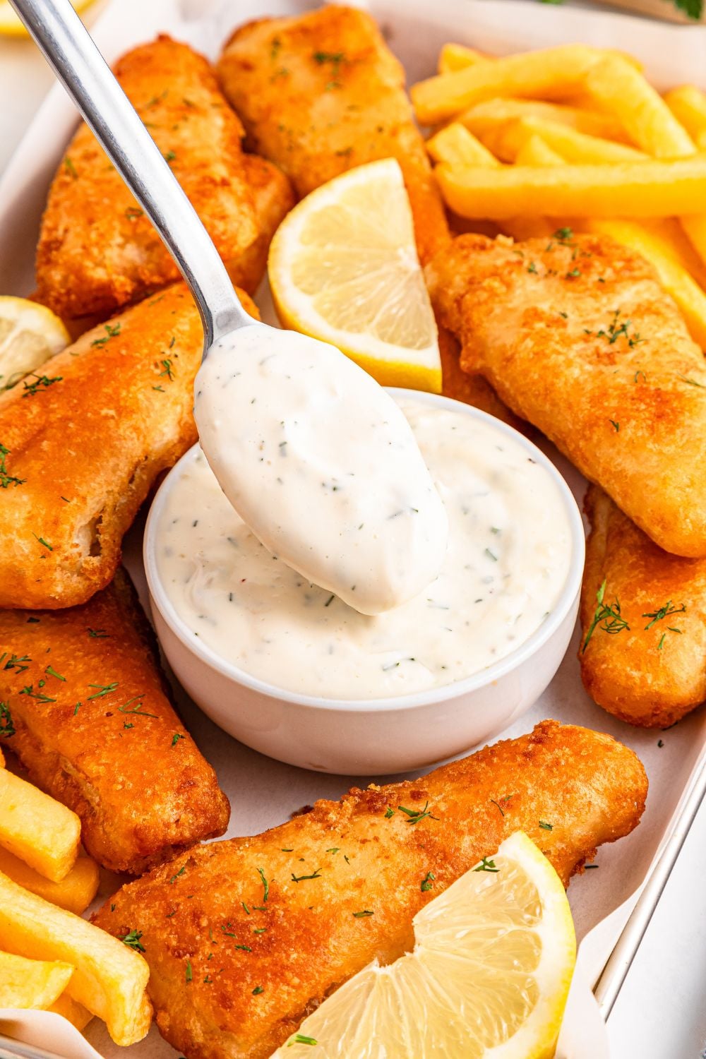 bowl with a spoon dipping in tartar sauce and fish fillets and fries