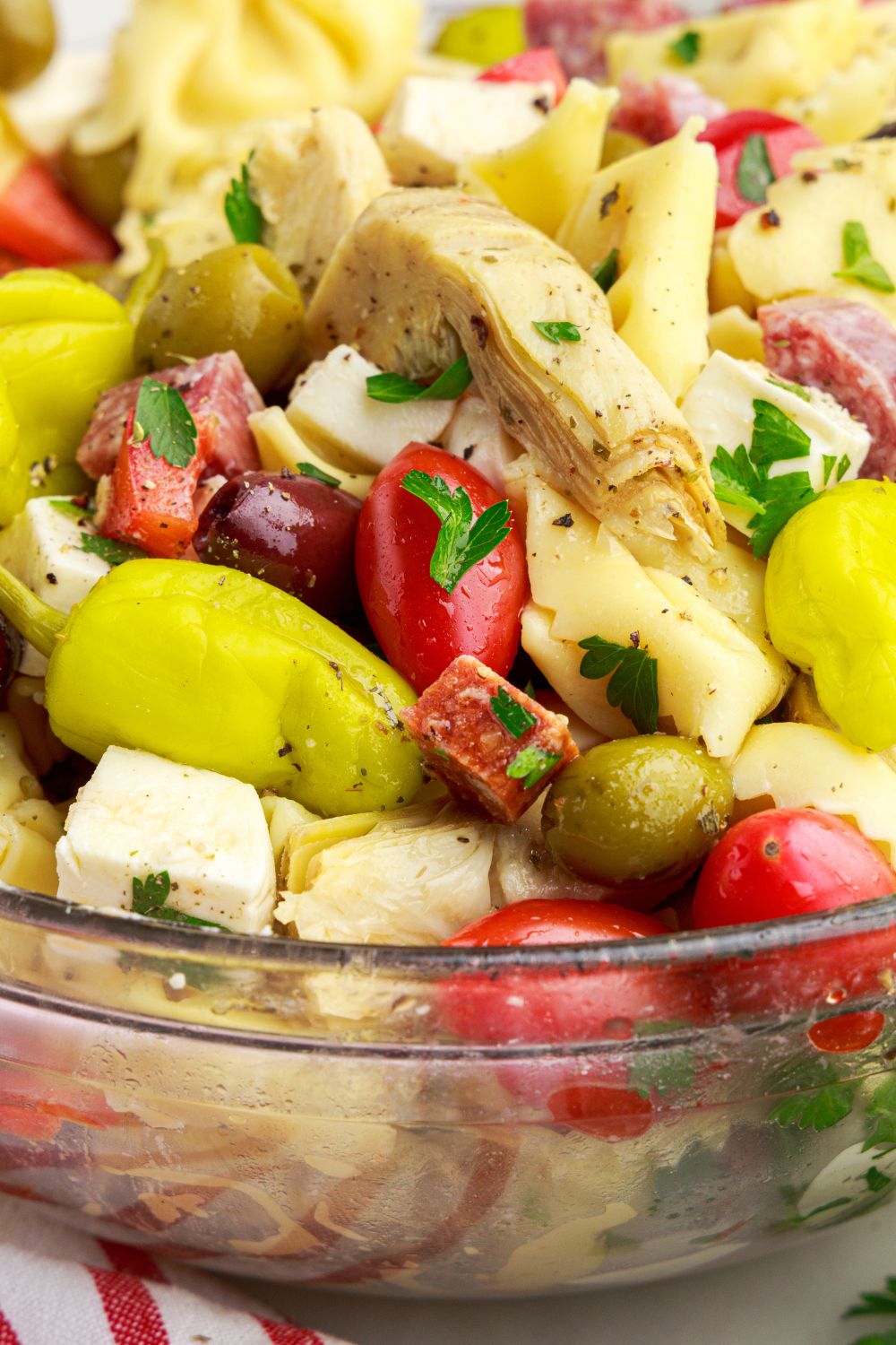 Antipasto Tortellini Pasta Salad in a bowl with close up of artichokes, peppers and more 