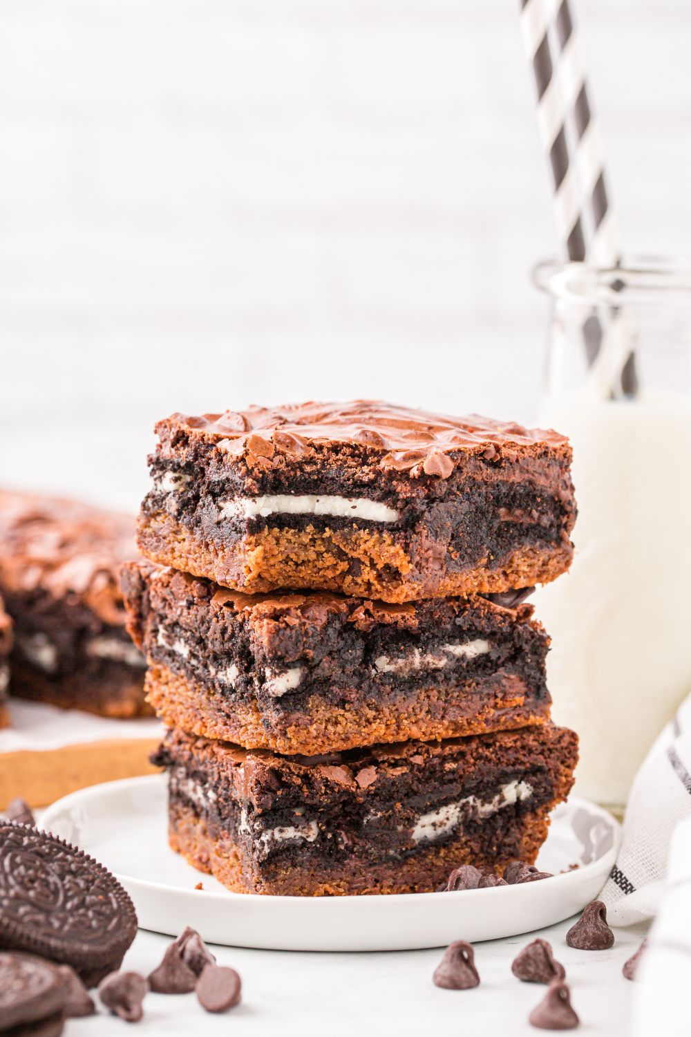 layered Slutty Brownies stacked on a plate with a glass of milk to side and more sliced bars on a tray