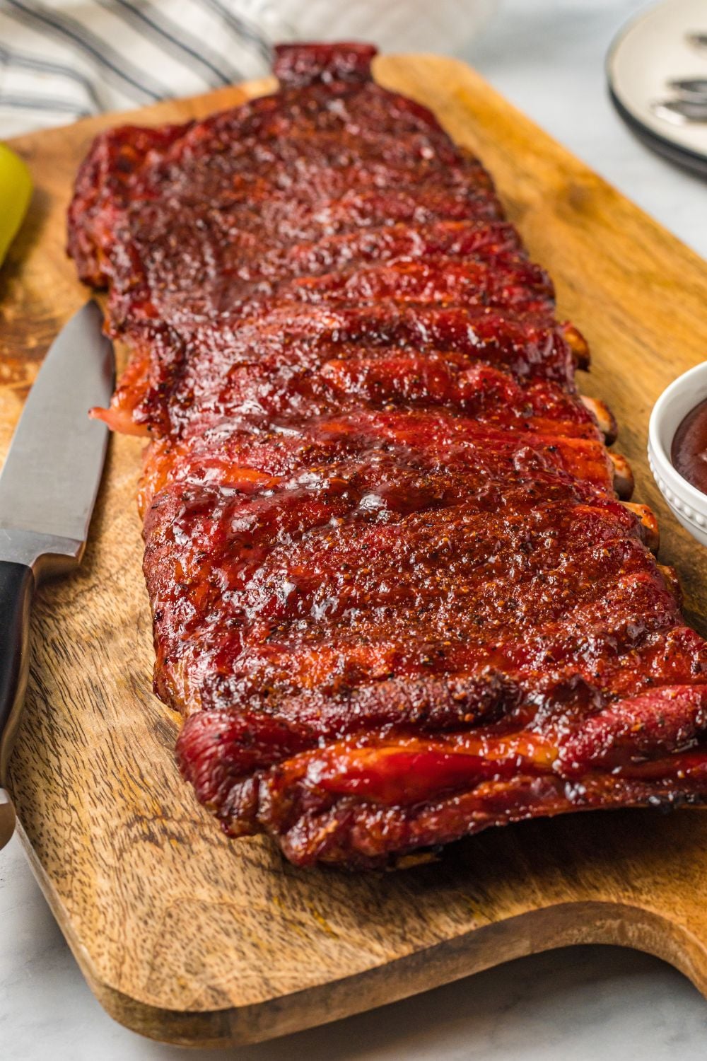 Grilled BBQ Baby Back Ribs on table with sharp knife to side and a bowl of bbq sauce