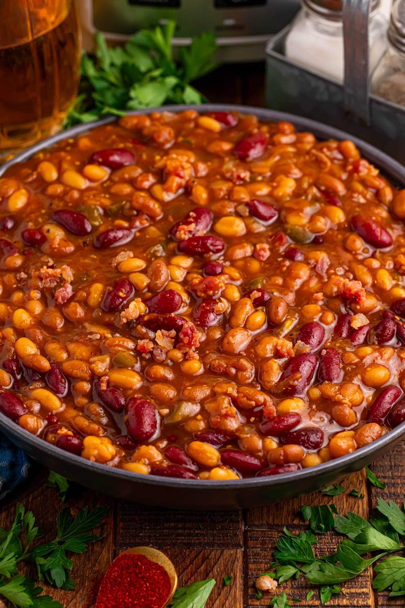 Crockpot Bourbon Brown Sugar Baked Beans in a bowl sitting on table with some fresh herbs to side of bowl