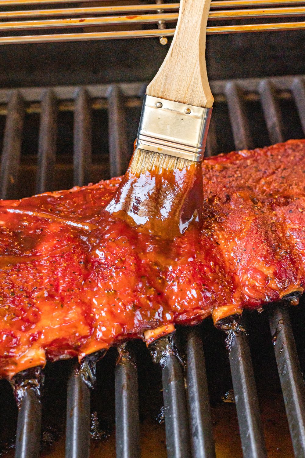 baby back ribs on grill being brushed with sauce