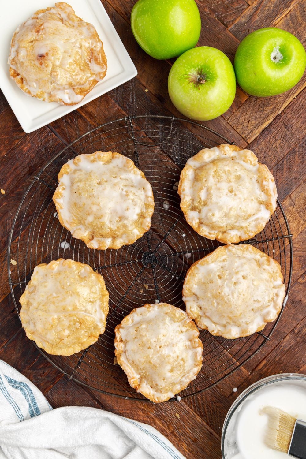 Deep Fried Apple Hand Pies spread around table with apples to side and a bowl of glaze to side